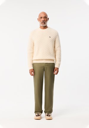 Crème gekleurde trui met een ronde hals, olijfgroene broek en tan sneakers met dierlijke prints.