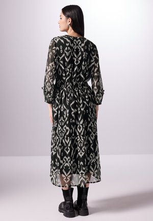 Černobíle vzorované maxi šaty s dlouhými rukávy, elastickým pasem a vrstvenou sukní, vyrobené z lehkého, průsvitného materiálu.