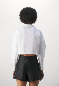 Afskåret hvid bomulds skjorte med klassisk krave, lange ærmer og manchetter; parret med højtaljede sorte shorts med lynlås.