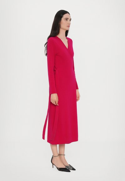 Rochie cu mâneci lungi, model petrecut, dintr-un material roz aprins, cu legături laterale. Însoțită de pantofi negri cu toc ascuțit și barete la nivelul gleznei.