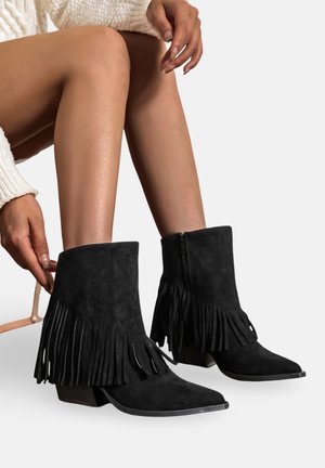 Bottes chelsea en suède noir avec des détails à franges, bout pointu et talon empilé. La fermeture éclair est située à l'arrière pour un enfilage facile.
