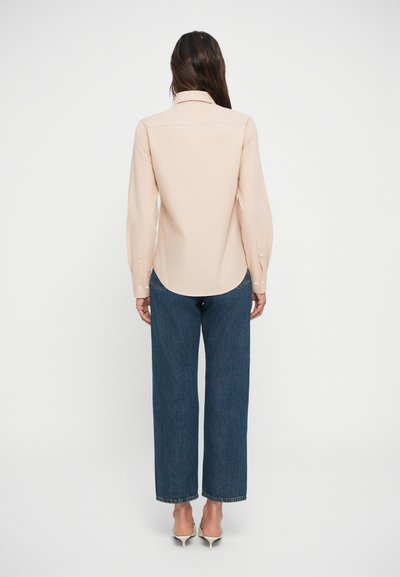 Light pink long-sleeve shirt with a collar, buttoned cuffs, and a rounded hem, paired with dark blue wide-leg jeans and light-colored heels.