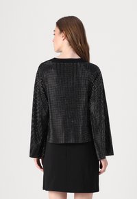 Juodas trumpas megztinis su ilgais rankovėmis, pasižymintis tekstūruota medžiaga, puoštu mažais sidabriniais taškais, ir apvalia iškirpte.