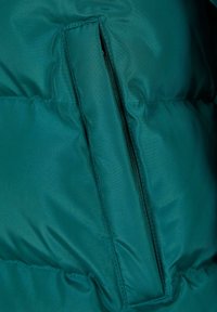 Teal puffer jacket section with a vertical zipper pocket. The fabric has a smooth, shiny texture with visible stitching and fill.