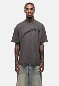 Grijze T-shirt met korte mouwen van katoen, met een donker bedrukt ontwerp van silhouetten aan de voorkant. Losse pasvorm met een ronde hals.