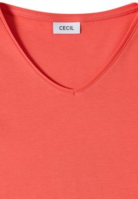 T-shirt rose corail à col en V avec des coutures visibles et une étiquette blanche indiquant "CECIL" au col à l'intérieur de l'encolure.