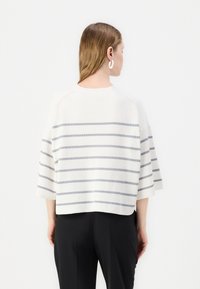Pulover alb scurt cu dungi orizontale gri, mâneci largi și decolteu rotund, îmbrăcat cu pantaloni negri. Material moale la atingere.