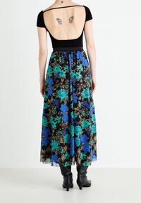 Svart topp med bred rygg, matchad med en blommig maxikjol med blå och gröna blommor på en svart bakgrund. Bärs med svarta knähöga stövlar.