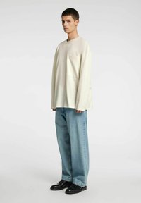 Langermet kremhvit skjorte med lomme, kombinert med lyseblå vide jeans og svarte sko, med et minimalistisk design og avslappet passform.