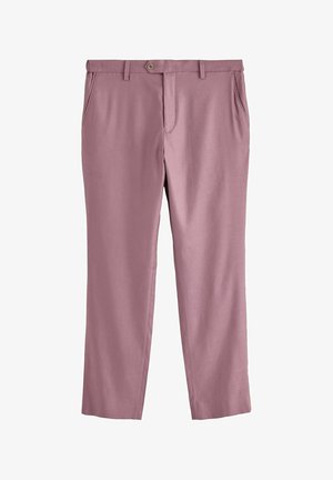 Linke Hand einer Person mit dunkler Haut neben der Taille, die hellviolette Hose und ein weißes Langarmshirt mit aufgekrempeltem Ärmel trägt.