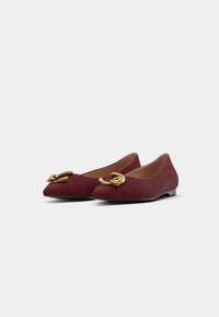 Sapatilhas de camurça burgundy com um design de bico apontado, apresentando um destacado embellishment de dupla argola dourada na parte frontal e uma sola plana.
