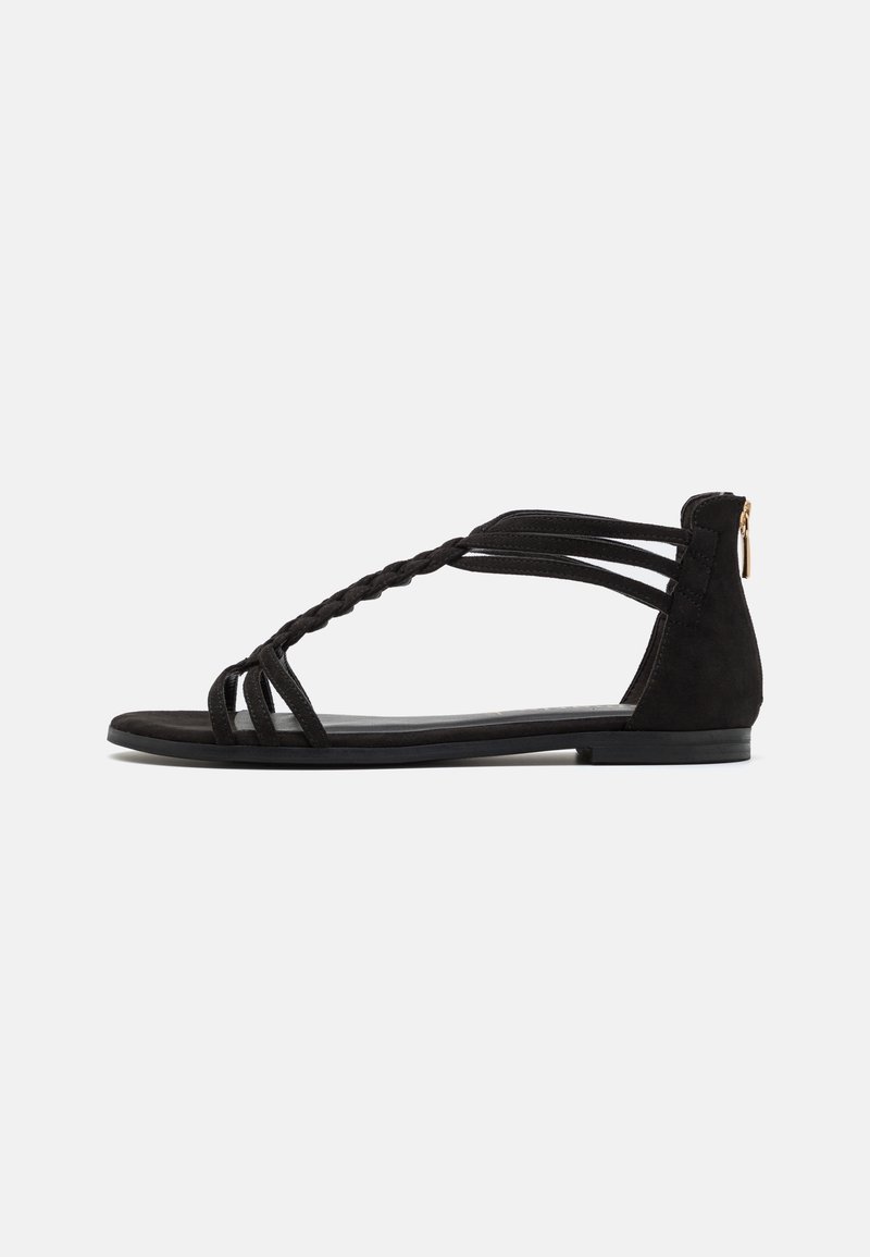 Sandales plates noires avec brides tressées, en suède, design à bout ouvert, fermeture éclair latérale et petit talon pour le confort.