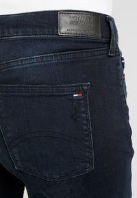 Tmavě modré džíny z denimu s texturovaným povrchem, zadní kapsa s jemným švem a kožený štítek s logem "TOMMY JEANS".