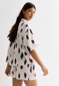 Korte mouw, crèmekleurige lounge-set met zwart penseelstrekenpatroon; losvallend shirt en bijpassende shorts van lichte, gestructureerde stof.