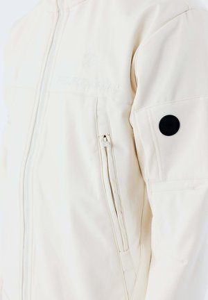 Veste blanc cassé avec fermeture éclair à l'avant, poche latérale zippée, logo brodé sur la poitrine et patch circulaire noir sur le haut de la manche.