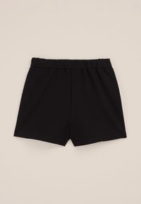Schwarze Baumwollshorts mit elastischem Bund flach auf einem hellbeigen Hintergrund ausgelegt, Vorderseite und glatte Stofftextur zeigend.
