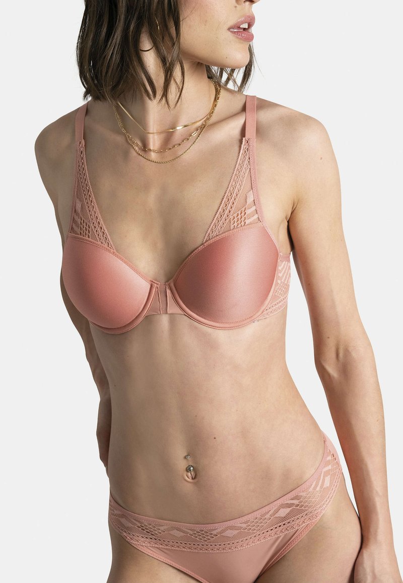 Soutien-gorge rembourré rose avec des détails en dentelle sur les bretelles, texture lisse et forme structurée. Assorti à des culottes avec des accents en dentelle.