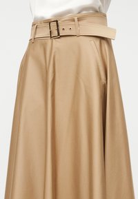 Μπεζ φούστα σε γραμμή A με φαρδιά ζώνη και ομαλή υφή. Διαθέτει πλαϊνή τσέπη και γυαλιστερά μεταλλικά στοιχεία στη ζώνη.