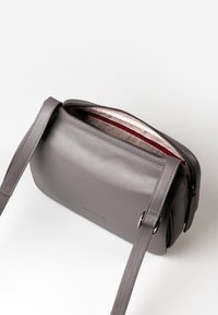 Borsa a tracolla in pelle grigia con una texture liscia, chiusura con zip e foderatura interna a fantasia. Presenta una tracolla removibile e dettagli cuciti.