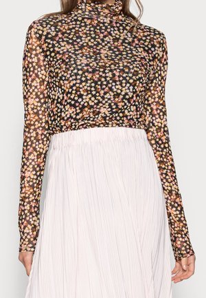 Haut à manches longues en tissu transparent noir, orné de petites fleurs roses, jaunes et blanches, associé à une jupe blanche plissée.