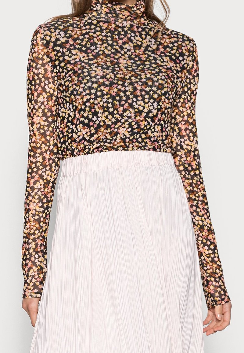 Top floreale a maniche lunghe in tessuto trasparente nero, decorato con piccoli fiori rosa, gialli e bianchi, abbinato a una gonna bianca plissettata.