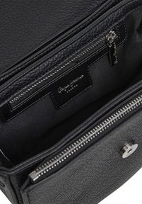 Interior de uma mala de couro preto texturizado, mostrando um bolso com fecho de correr e puxador metálico, além de um fecho magnético no flap frontal.