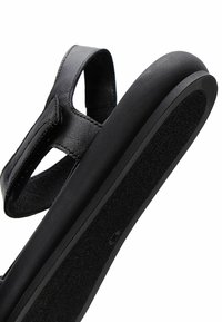 Sandale orthopédique noire avec bride réglable et semelle rembourrée, conçue pour le soutien et le confort du pied.