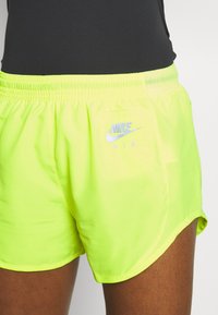 Pantalones cortos Nike de neón amarillo con cinturilla elástica. Presentan el logo "NIKE AIR" en gris claro en el lado izquierdo. Tejido liso y ligero.