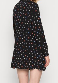 Czarna sukienka o luźnym kroju, z kolorowym, rozproszonym wzorem w krople. Długie rękawy i kołnierzyk, gładki materiał.