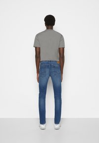 Camiseta gris de manga corta combinada con jeans ajustados de color azul oscuro. La camiseta tiene un cuello redondo y los jeans presentan una etiqueta de parche en la parte trasera.