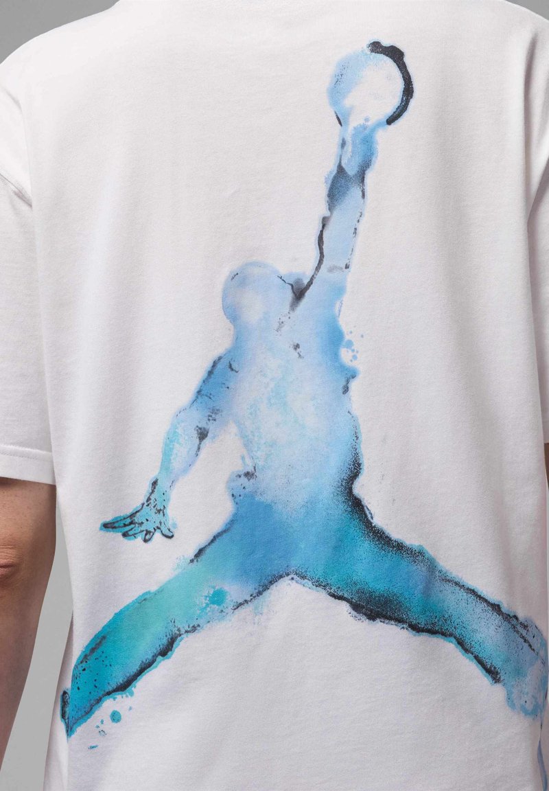 Silueta en acuarela azul de un jugador de baloncesto saltando y alcanzando la pelota en la parte posterior de una camiseta blanca.