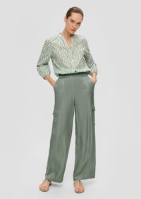 Lichtgroene blouse met een geometrisch patroon en lange mouwen, gecombineerd met lichtgroene wijde cargobroeken met zijzakken.