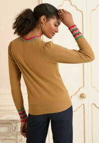 Bruine gebreide trui met gestructureerde mouwen en golvende rode, groene en roze accenten bij de manchetten en de halslijn. Slim fit en geribde zoom.