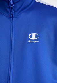 Zila zipa jaka, kas izgatavota no gludas, elastīgas auduma. Tam ir balts "Champion" logo uz krūtīm un plānas baltas svītras uz pleciem.