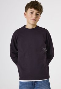 Donkerpaarse T-shirt met lange mouwen, ronde hals en witte geborduurde tekstpatroon op de borst. Draag het met lichtblauwe spijkerbroek.