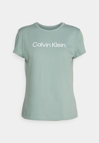 Camiseta de algodón verde claro con cuello redondo. Presenta un logo de texto blanco "Calvin Klein" en el pecho. Mangas cortas, textura suave.