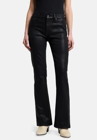 Czarne dzwony uszyte z gładkiego, elastycznego materiału mają kieszenie z przodu, zamek błyskawiczny oraz dopasowaną talię. Noszone z beżowymi szpilkami.