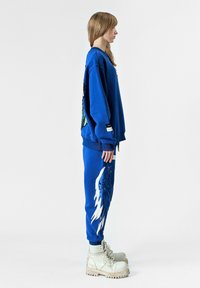 Sudadera azul con gráfico de mariposa y pantalones blancos con diseño de alas azules; combinados con botas de cordones color crema.