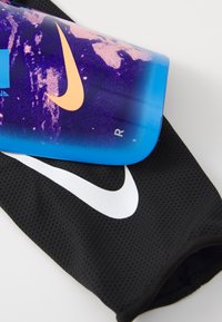 Bouteille d'eau de sport Nike avec un dégradé bleu orné de motifs violets et un swoosh orange, placée sur une housse en maille noire avec un logo blanc.