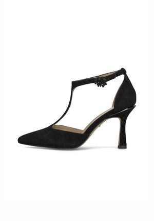 Zapato de tacón alto de ante negro con tira en T y puntera puntiaguda, decorado con una pequeña hebilla floral negra en la tira lateral.