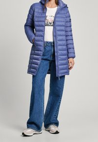 Ljuslila puffjacka med huva, med en quiltad design och full dragkedja. Kombineras med vida denimjeans och sneakers.