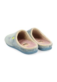 Chaussons en fausse fourrure de couleur bleu clair avec une doublure beige, forme arrondie, texture douce, et une semelle intérieure rose arborant une étiquette de marque.