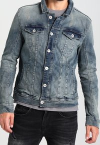 Džínová bunda ve vybledlé modré barvě s předními kapsami, zapínáním na knoflíky a texturovaným povrchem. Má slim fit střih a kontrastní prošívání.