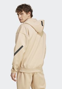 Um hoodie bege claro com um tecido texturizado, apresentando um capuz, ombros caídos e um detalhe de faixa preta na manga.