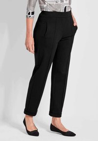 Zwarte tapering broek met een brede elastische tailleband, zijzakken en opgerolde manchetten, gecombineerd met zwarte platte schoenen. Glad stofmateriaal.