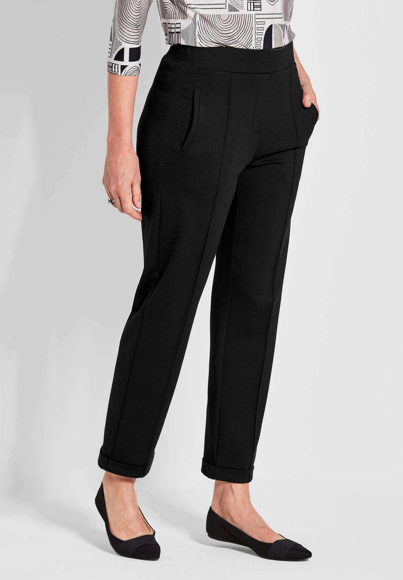 Zwarte tapering broek met een brede elastische tailleband, zijzakken en opgerolde manchetten, gecombineerd met zwarte platte schoenen. Glad stofmateriaal.