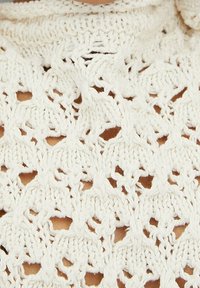 Bílá pletená tkanina se složitým vzorem s otevřenou strukturou, zahrnující diamantové tvary a malé dírky, které vytvářejí texturovaný a lehký vzhled.