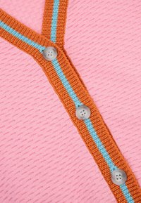 Roze gestructureerde stof met een oranje en blauwe gestreepte gebreide rand, met drie grijze knopen langs de rand.