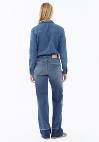 Denim shirt and flared jeans in mid-wash blue. Shirt features a collar and button closure; jeans have back pockets and subtle stitching details.