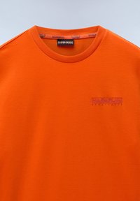 Orange bomulds T-shirt med rund halsudskæring, der har et subtilt præget logo i lilla på brystet. Glat tekstur, afslappet design.